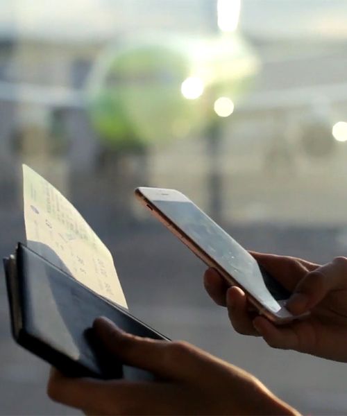 Up-close photo of a person holding a cellphone and plane boarding pass, the screen of the phone is not visible